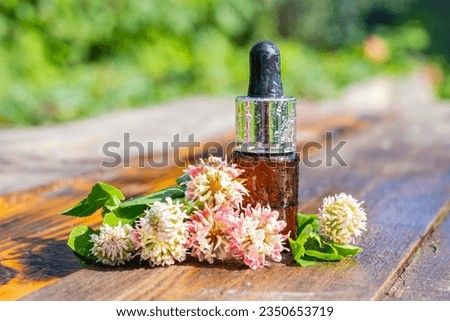 A bottle with a pipette and oil, clover flowers on a wooden background. Bubbles with oil and clover flowers. Clover oil in a bottle. Clover essential oil in a small bottle. Selective focus.