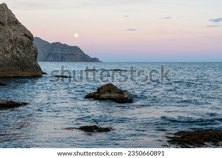 Sudak, Crimea. Moon rise. Cape Rybachy. Mount Meganom in the light of the setting sun