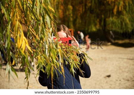 The girl takes pictures on the phone from behind the branches of a willow. Portrait of a girl