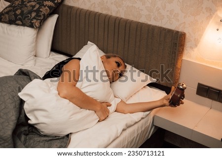 A woman is lying in bed with an alarm clock in her hands. Getting up early for work. High quality photo