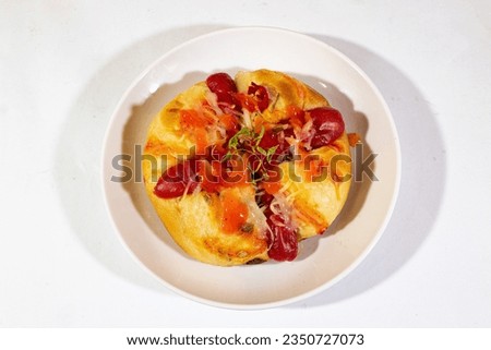A plate of smoked bread garnished with sausage and tomato sauce is placed in the middle of the object pictured from above