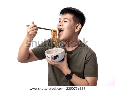 A portrait of a happy Asian man wearing a green army-colored shirt while eating noodles. Isolated against a white background