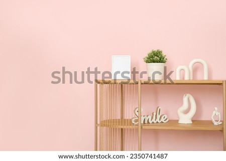 Wooden shelving unit with blank frame and decor near pink wall