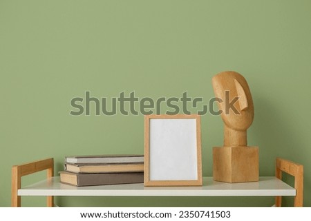 Blank frame with books and decor on shelf near green wall, closeup