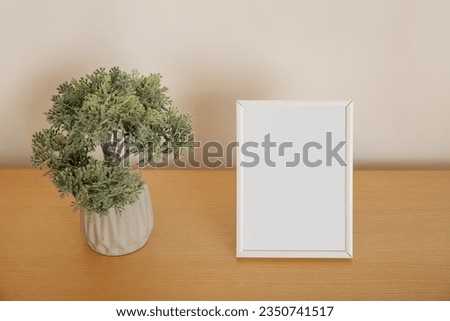 Blank frame and decorative tree in pot on wooden table, closeup