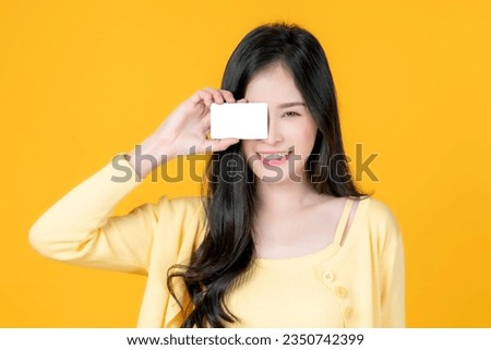 Asian woman cute girl holding and showing empty business card , credit card or name card - for payment shopping online and - paying by credit card isolated on yellow - business concept