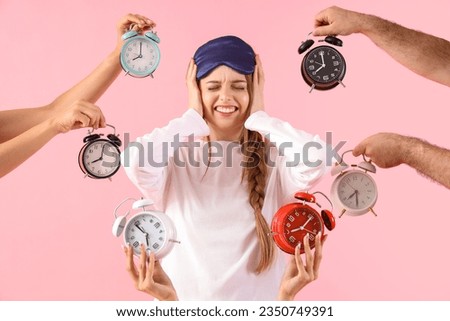 Young woman surrounded by loud alarm clock on pink background Royalty-Free Stock Photo #2350749391