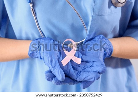 Female doctor with pink ribbon on light background, closeup. Breast cancer awareness concept
