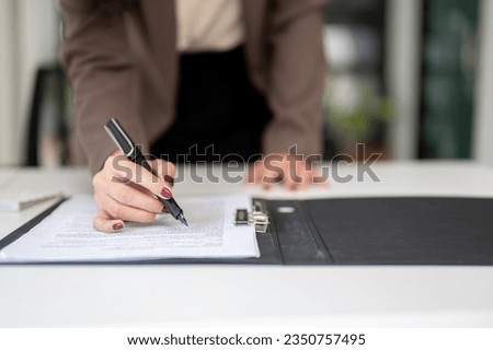 Close-up image of a businesswoman reading documents or a contract, signing her signature on a contract agreement at her desk.