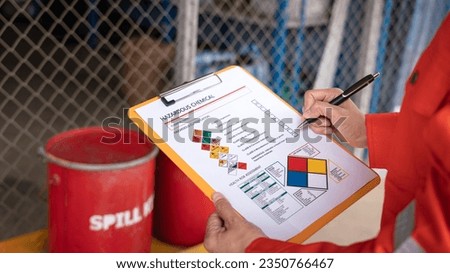 Action of safety officer is checking chemical hazard material form for correct the oil spill kit which is placed at front of chemical storage warehouse area in factory. Close-up and selective focus. Royalty-Free Stock Photo #2350766467