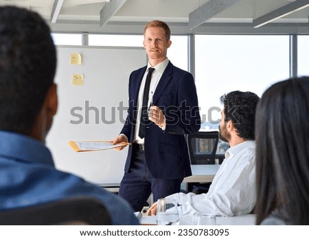 Business man presenter team leader wearing suit giving presentation training on whiteboard in office. Male company executive manager presenting corporate strategy at group conference meeting.