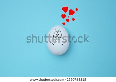 White egg with a surprised expression with red hearts above it. Copy space. Emoticons concept. Art collage