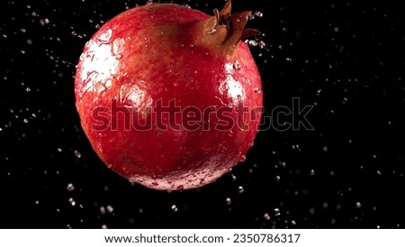 Pomegranate with drops and splashes water on black and white background, studio lighting