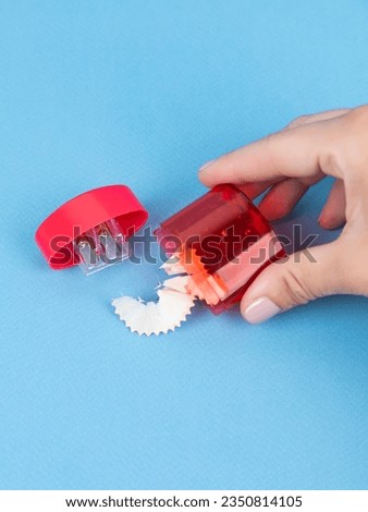 Close-up of a young woman sharpening a training slate pencil in a  red plastic sharpener on a blue background