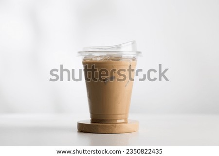 Iced cappuccino in a plastic glass on a white wooden table, minimalist-style picture.