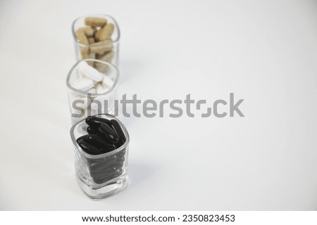 medicines in a glass, vitamins on a white background, vitamins on the table, insomnia, a bunch of drugs, medicines for insomnia, white black and brown pills in a glass, on a white background, a crossw