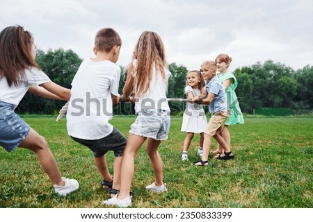 Holding the rope, playing game. Kids are having fun on the field at daytime together. Royalty-Free Stock Photo #2350833399