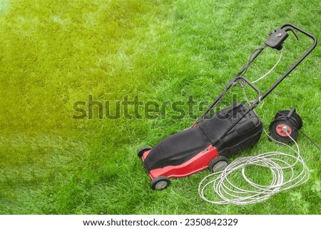 red electric lawn mower on a green lawn with wires and an electric extension cord, portable socket Royalty-Free Stock Photo #2350842329