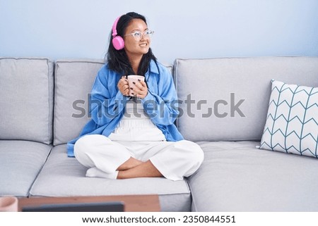 Young chinese woman listening to music drinking coffee at home