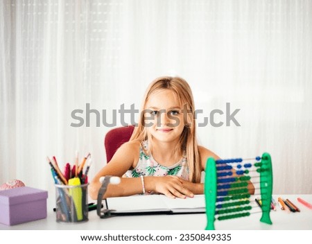Cute blonde girl sitting at her desk at home and and looks at the camera	