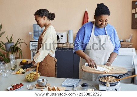 Portrait of two black young women preparing meals together cooking in kitchen Royalty-Free Stock Photo #2350852725