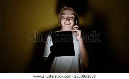 Young blonde woman using touchpad talking on smartphone over isolated yellow background