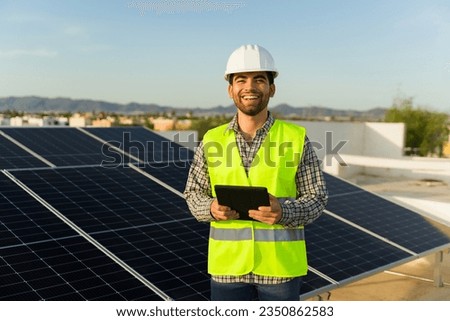 Cheerful latin engineer working with power generation and solar panels using the tablet during energy monitor Royalty-Free Stock Photo #2350862583
