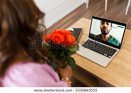 Romantic woman receiving flowers from her long-distance boyfriend blowing a kiss on the laptop screen during a video call