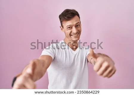 Caucasian man standing over pink background approving doing positive gesture with hand, thumbs up smiling and happy for success. winner gesture. 