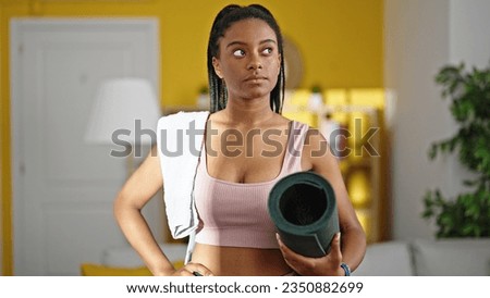 African american woman wearing sportswear holding yoga mat at home