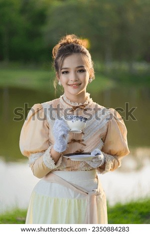 Beautiful Asian girl in the Victorian or Edwardian era dressed relaxed and having a happy afternoon tea party in nature on the river bank, enjoying picnicking, reading books, and sipping tea.