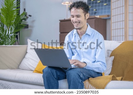 Businessman smiling sitting on home house indoor modern sofa using laptop technology, entrepreneur adult man male person using wireless internet connection working notebook in business communication