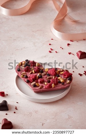 Valentine's day chocolate heart with raspberries on a pink background. Minimalistic composition. Extra dried raspberries and chocolate scattered on the background. Royalty-Free Stock Photo #2350897727