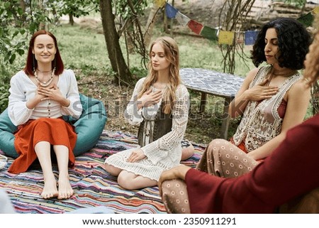 young woman meditating near smiling and multiethnic girlfriends on meadow in retreat center