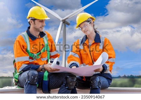 Team of male and female engineers with blueprint of wind turbines at windmill field farm. Group of engineers workers working at wind turbines farm. Alternative energy, environmental friendly.