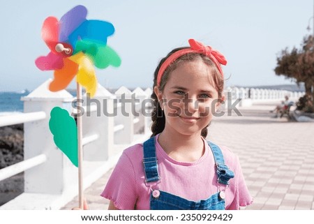 Blue-eyed girl holding a moving colored windmill. Concept: lifestyle, beach day, walk by the sea Royalty-Free Stock Photo #2350929429