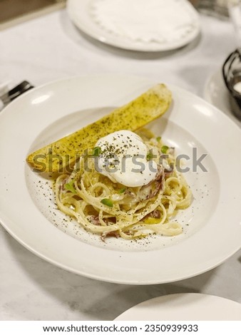 It's a picture of spaghetti carbonara, dry bread, white plate, egg , parsley leaf, slice beef
