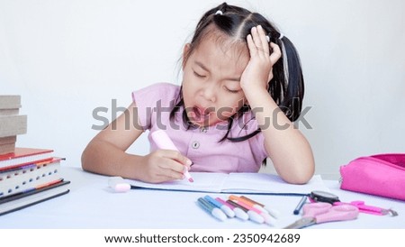 Portrait Of Sleepy Little Asian Female Child At Desk Tired After Doing School Homework.