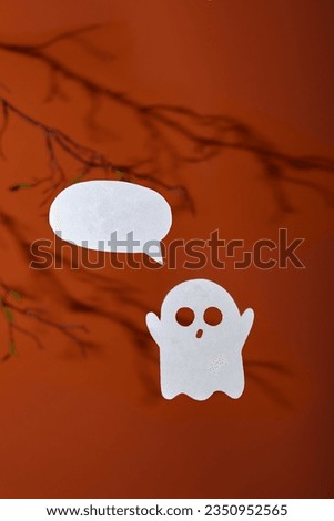 White paper ghost with a bubble for text on an orange background with shadows of tree branches