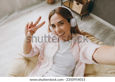 Close up young woman wear casual clothes headphones sits in armchair do selfie shot pov mobile cell phone listen music stay home hotel flat rest relax spend free time in living room. Lounge concept