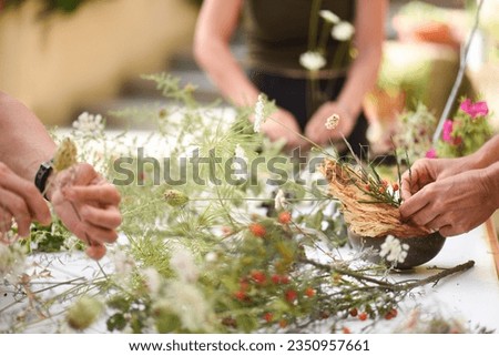 Detail of hands making flower arrangement, outdoor ikebana workshop, different flower arrangements in progress.