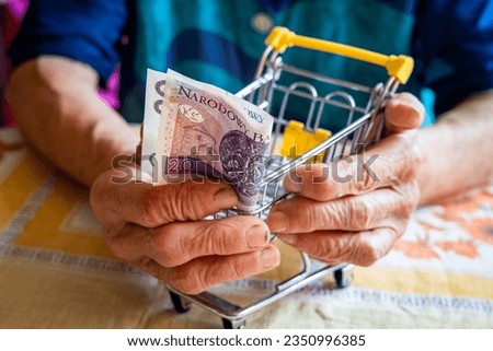 A Polish pensioner holds a thumbnail of an empty shopping trolley and 20 Polish zlotys in her hands, The concept of low pensions in Poland and rising food and fees Royalty-Free Stock Photo #2350996385
