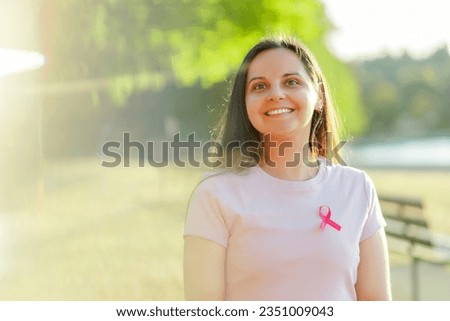 Portrait of beautiful smiling woman posing with pink ribbon on street. Young lady posing for picture. Breast cancer awareness month concept