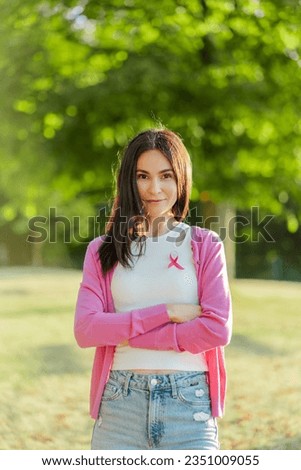 Happy confident middle aged woman with pink ribbon on t shirt looking at camera at the street. Breast cancer awareness month concept