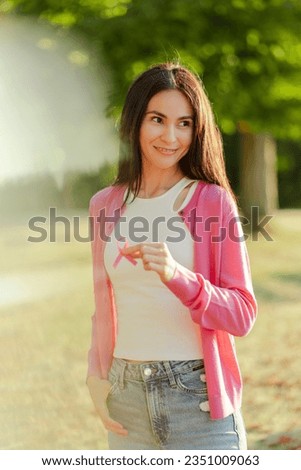 Portrait of beautiful smiling woman posing with pink ribbon on street. Young lady posing for picture. Breast cancer awareness month concept