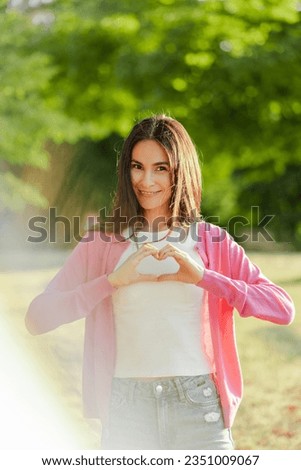 Confident woman in pink sweatshirt, holding hands in heart shape, smiling looking at camera at park. Breast cancer awareness day, cancer campaign, pink october 1st