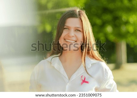 Smiling confident middle aged woman with pink ribbon on t shirt looking at camera at the street. Breast cancer awareness month concept