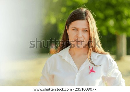 Happy confident middle aged woman with pink ribbon on t shirt looking at camera at the street. Breast cancer awareness month concept