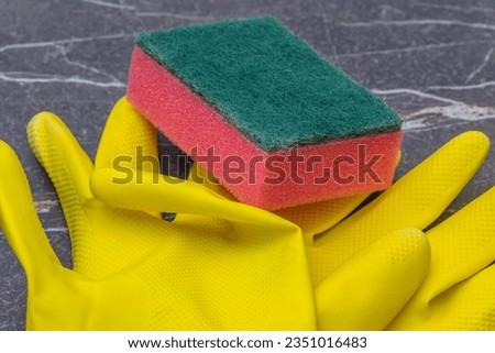 close up yellow household rubber gloves with red scouring pad on a marble background