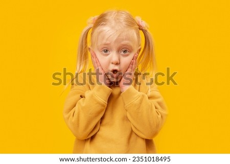 Portrait of cute blonde girl with two tails in isolation on yellow background. Emotion of surprise. Hands near open mouth